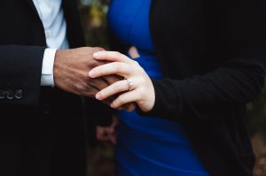 Close up of couple holding hands at a vow renewal ceremony. The woman wears an engagement ring.