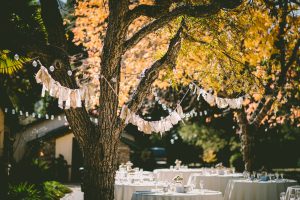 Photo of an evening wedding meal setting before the guests arrive, with bunting in the trees.